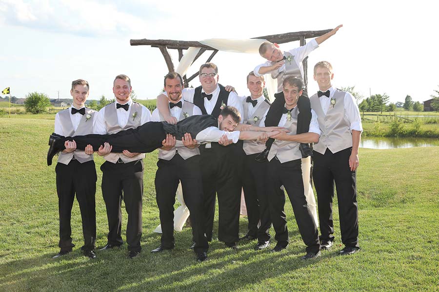 fun wedding party photo of the groom and his groomsmen holding one of the groomsmen on the golf course after the wedding at Stone Ridge Golf Club in Bowling Green, OH