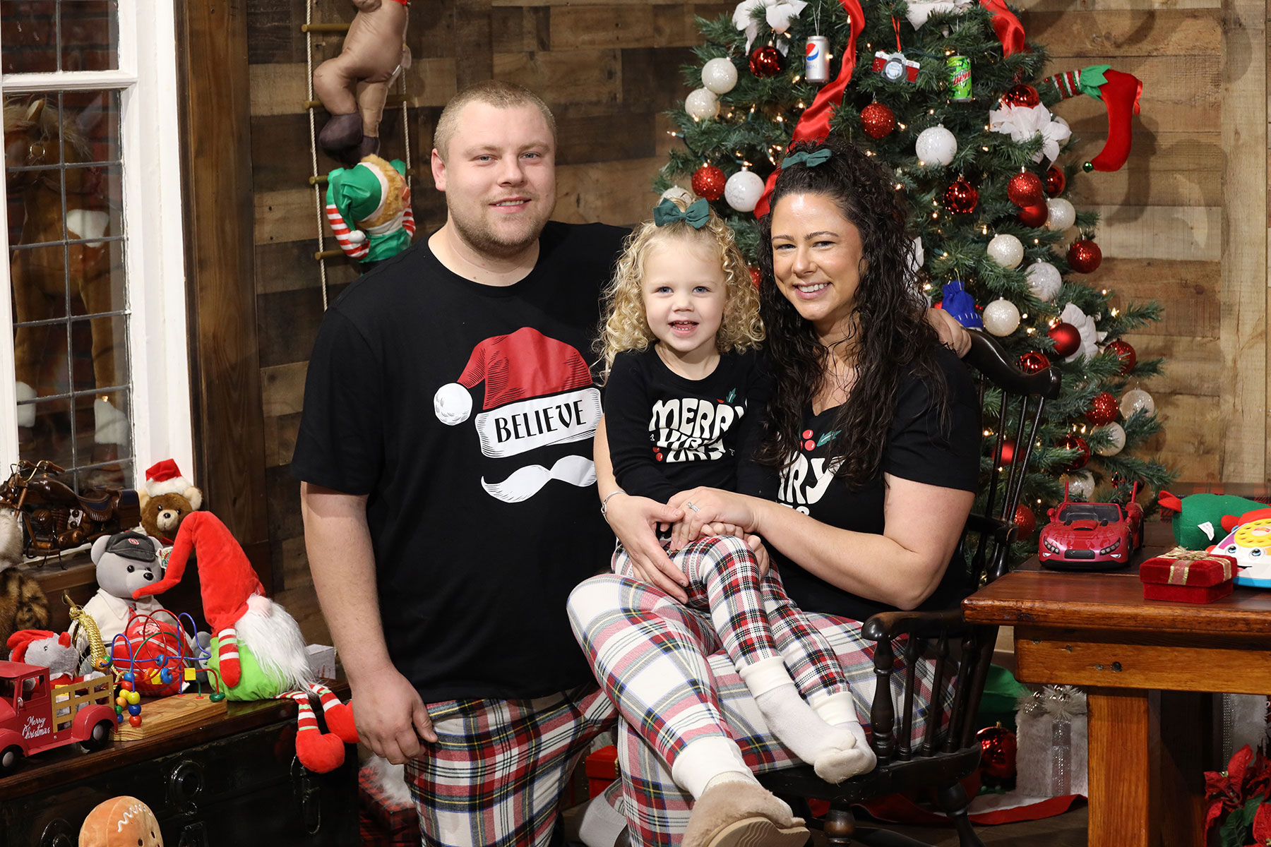 mom, dad, and little daughter posing for a photo near a christmas tree while wearing christmas pajamas