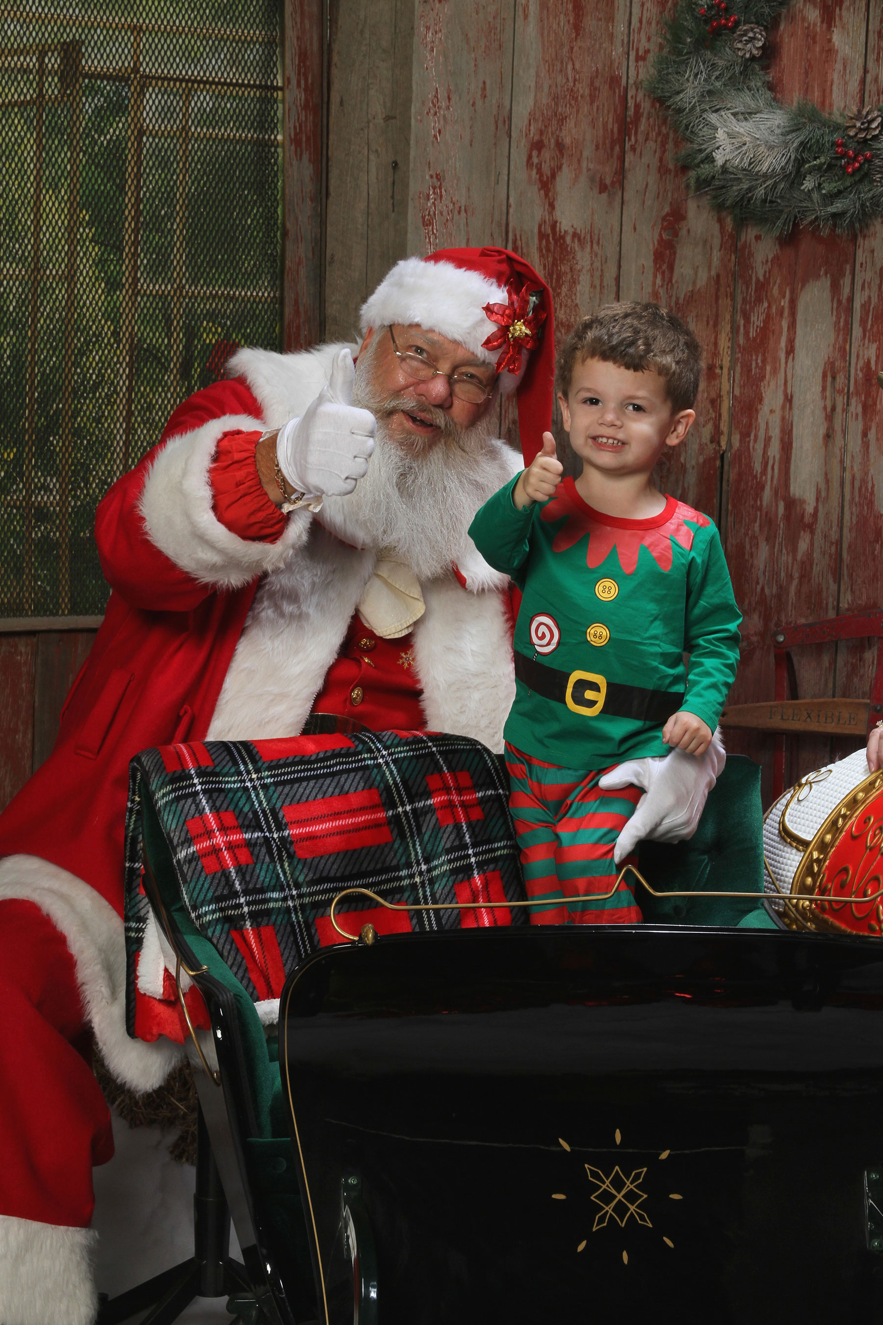 Santa and a little boy standing in his sleigh posing with their thumbs up 