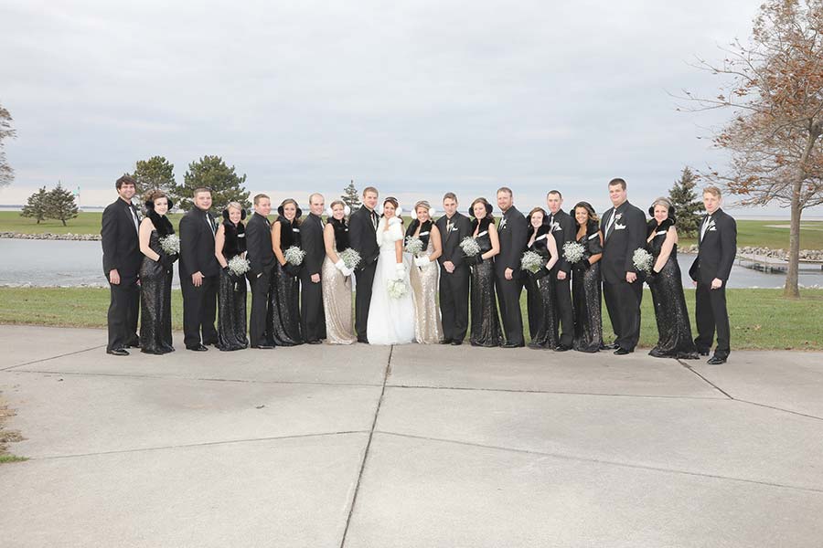 the wedding party dressed in long black gowns and black tuxes pose for a picture on New Year's eve at Maumee Bay State Park
