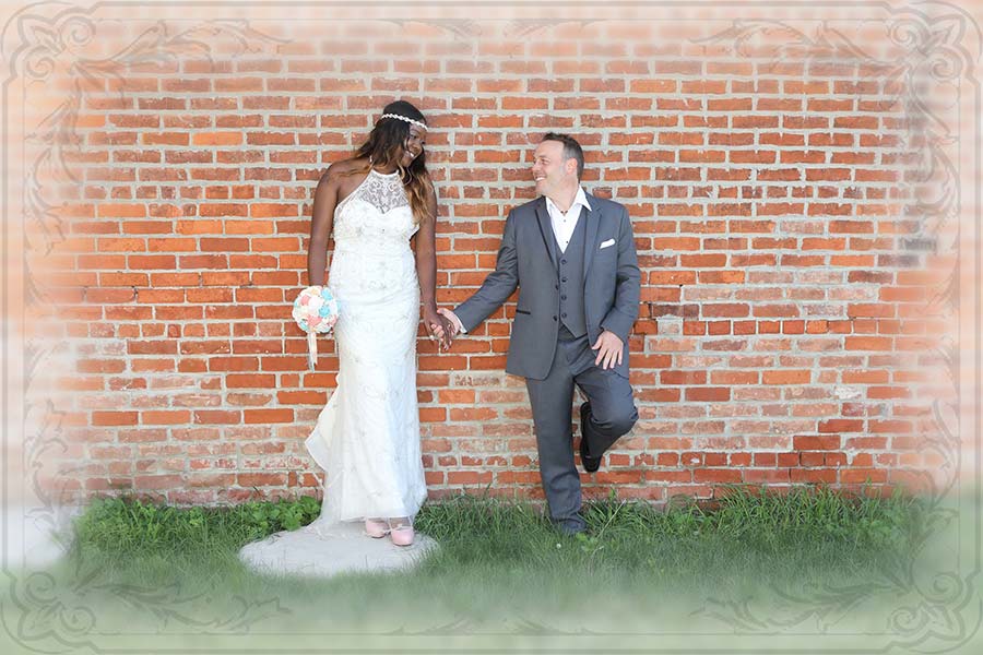the bride and groom holding hands while looking at one another and leaning against a brick wall in Bowling Green Ohio