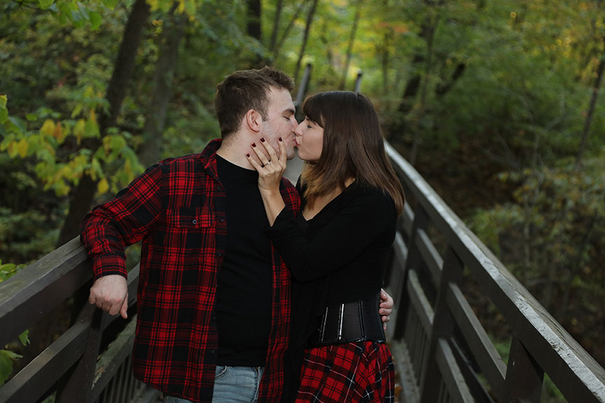 young engaged couple kissing while standing on the boardwalk behind the manor house at Wildwood MetroPark