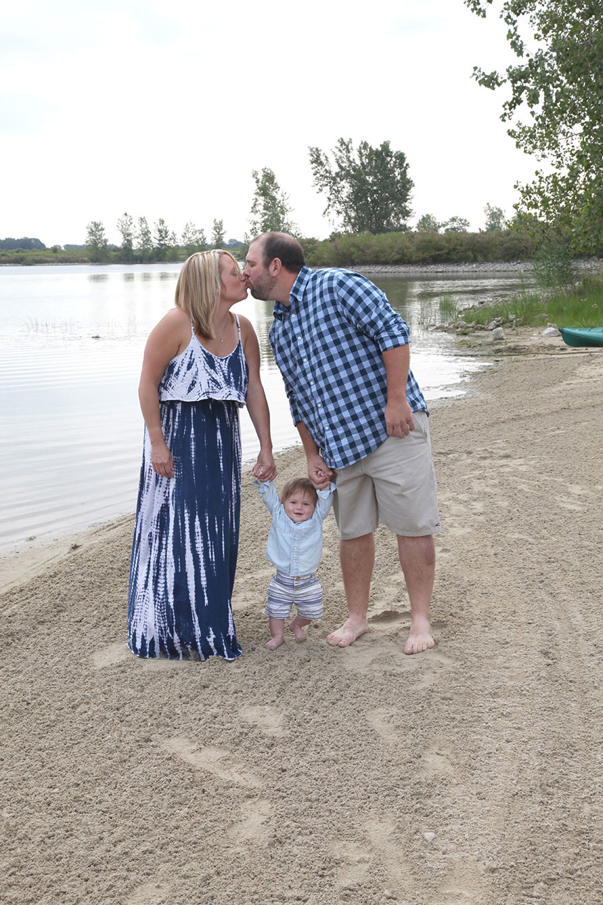 portrait of an engaged couple walking along the beach at Maumee Bay State Park with their baby and stopping for a kiss