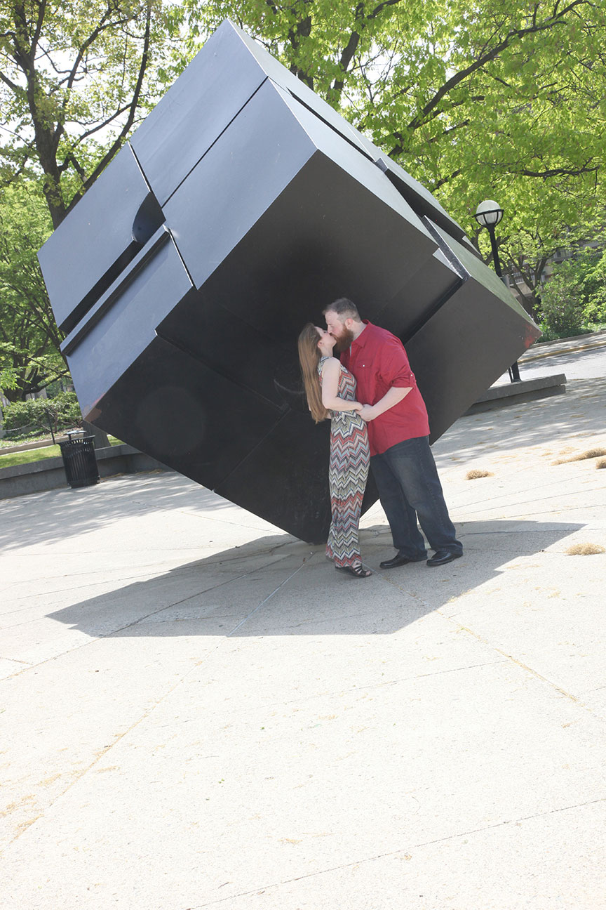 engaged couple pose for a kissing photo near the Tony Rosenthal Endover Cube at Regents' Plaza at the Univeristy of Michigan in Ann Arbor