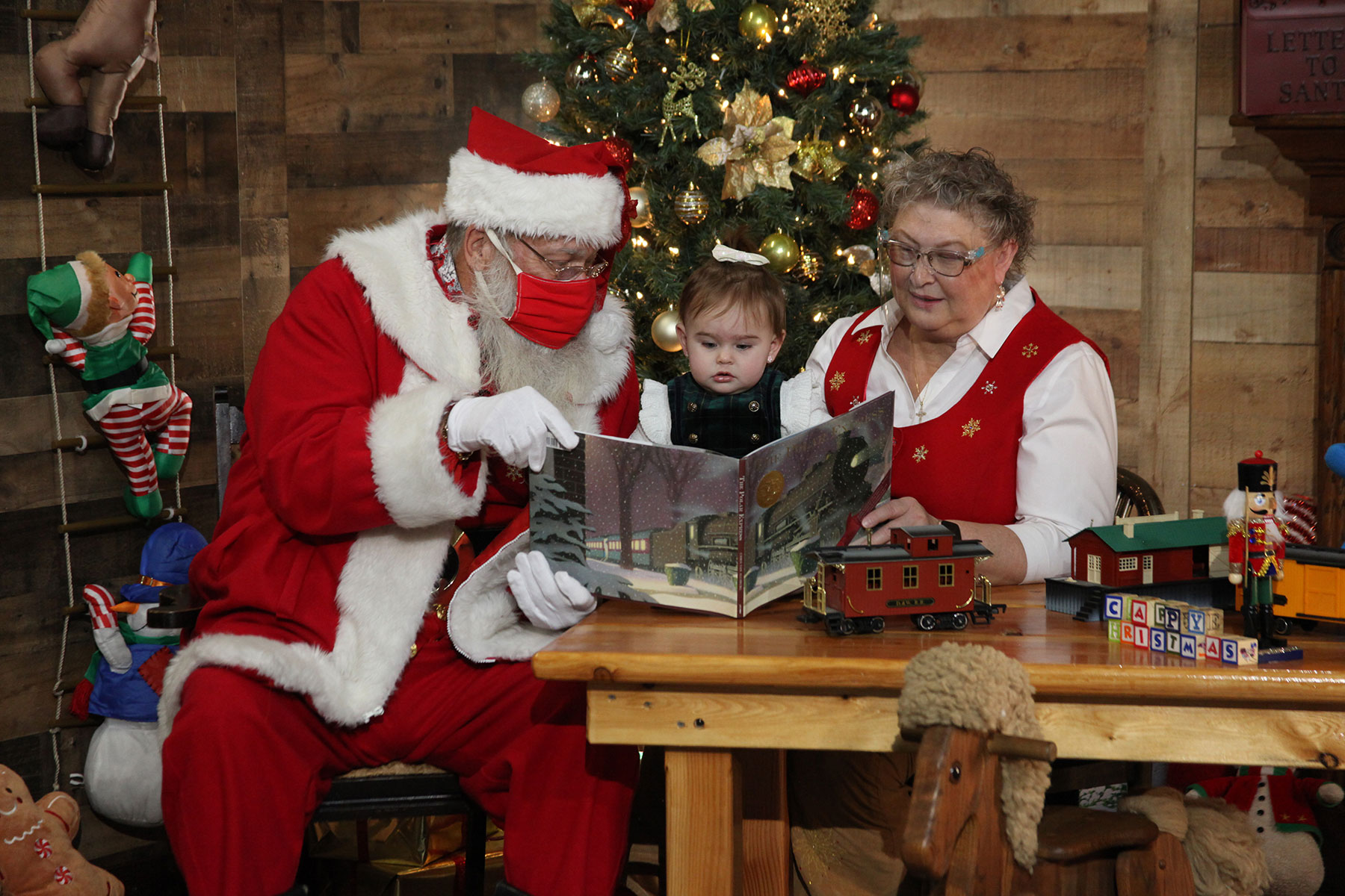 Santa and Mrs. Claus reading a book to a baby girl