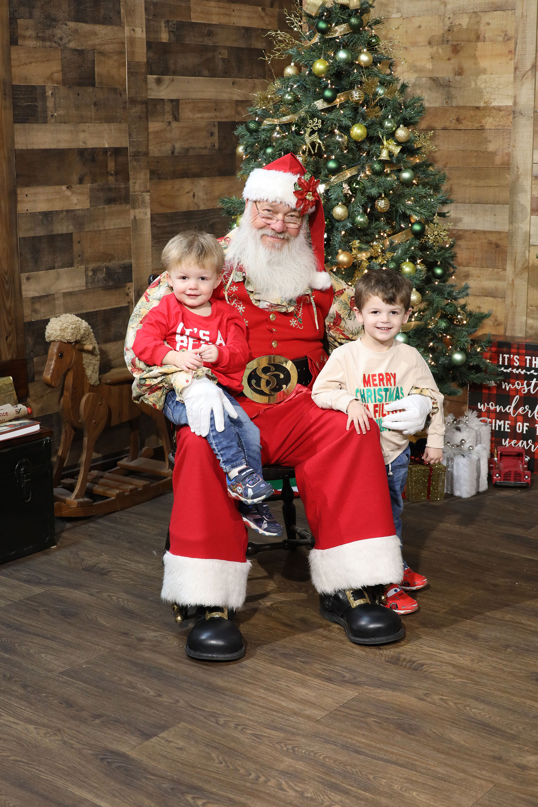 a little boy sitting on Santa's lap with his brother standing next to santa and posing for a photo at Kurt Nielsen Photography photo studio in Sylvania, Ohio