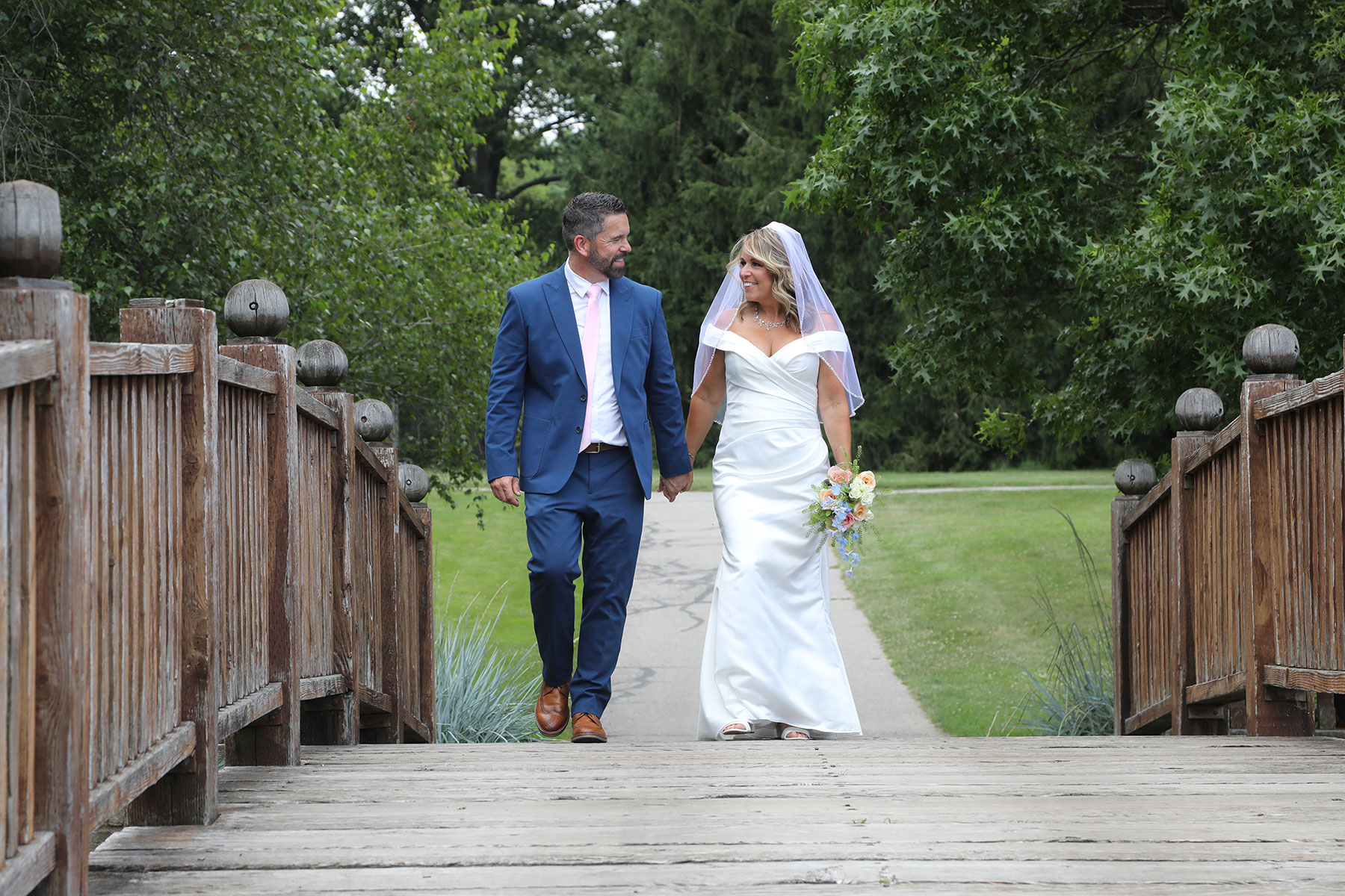 Toledo Botanical Wedding Photographer -  newly married couple walking hand in hand across the bridge at Toledo Botanical Gardens